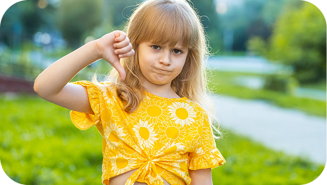 PBR Blog Young girl with blonde hair wearing a sunflower-patterned yellow shirt gives a thumbs-down gesture outdoors on a sunny day with green grass and trees in the background.