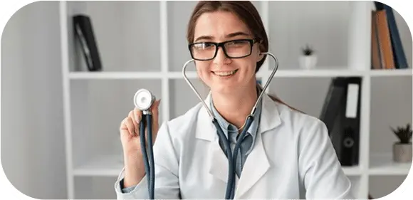 PBR QUESTION BANK Smiling female doctor wearing glasses and a white coat holds a stethoscope in a modern office setting with shelves and books in the background offering a welcoming atmosphere.