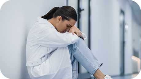 PBR Blog Doctor sitting on the floor in hospital hallway looking overwhelmed and exhausted symbolizing fatigue in healthcare professionals and the toll of medical responsibilities.