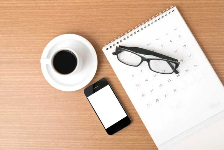 Coffee cup smartphone and glasses on a calendar placed on a wooden desk perfect for productivity planning and time management inspiration for a busy professional workspace.