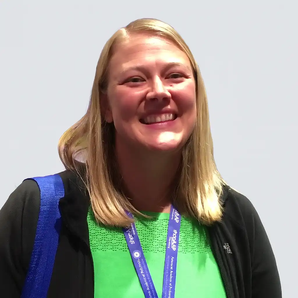 Home Smiling Dr. Jessie Maxwell at a conference, wearing a green top and a blue lanyard.