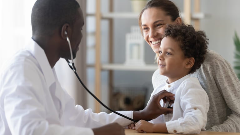 Doctor listening to a child’s chest with a stethoscope during a pediatric check-up as the parent looks on