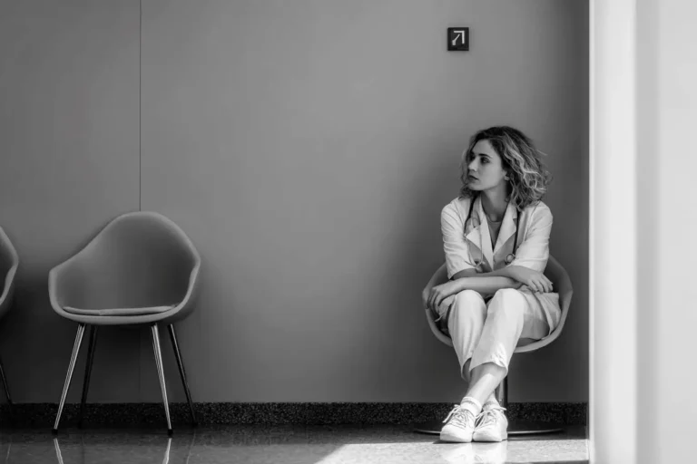 Pediatrician sitting quietly in a hallway, reflecting on the emotional weight of failing the pediatric boards and questioning what it means for their career