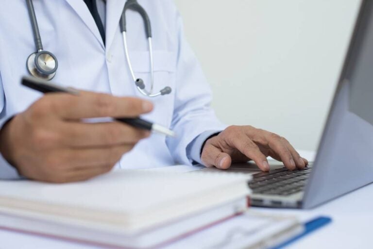 Physician studying and reviewing materials to prepare for the pediatric board exam using a laptop and notes.