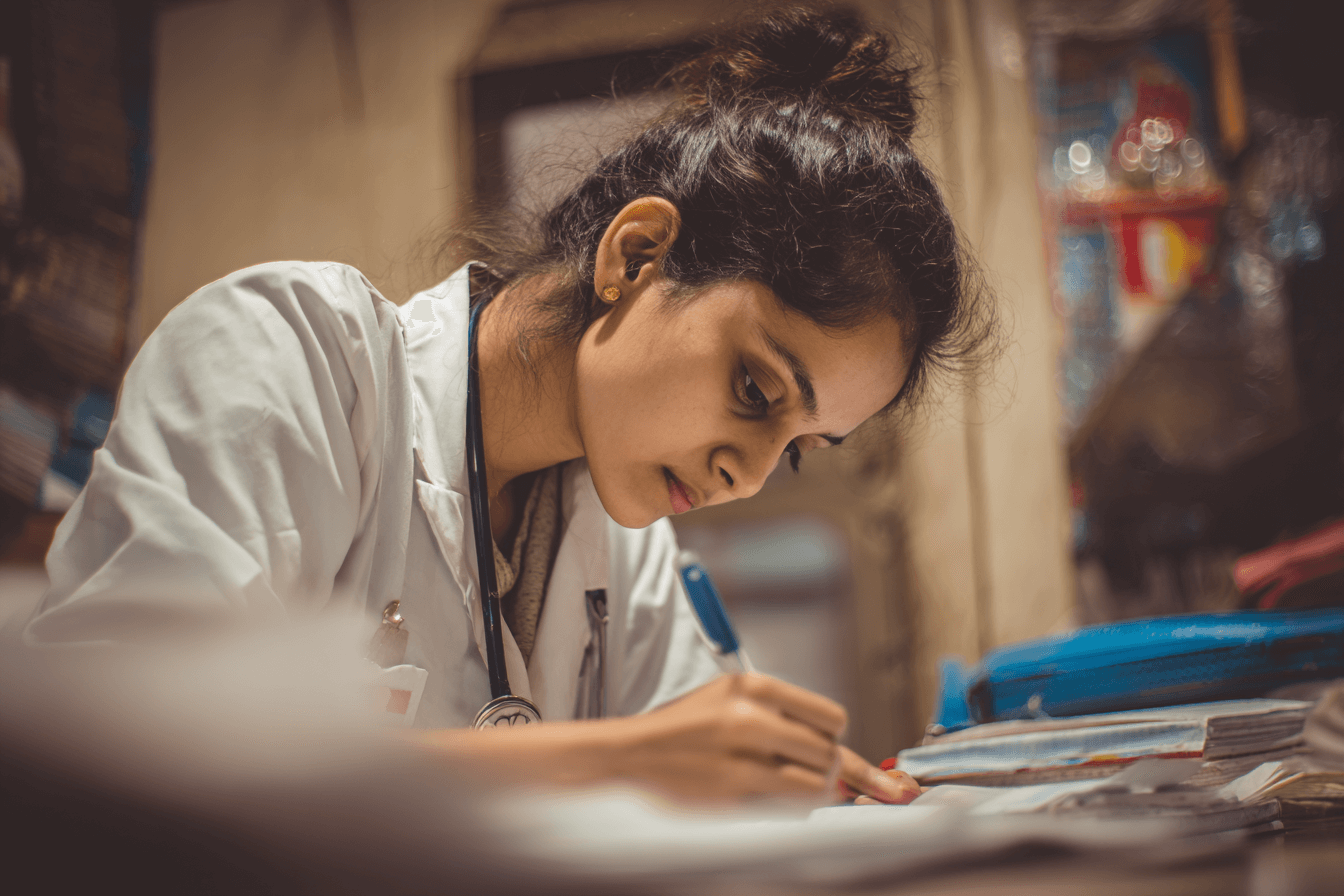 Focused first-time pediatric board exam taker in a white coat, studying intently with determination and exhaustion.